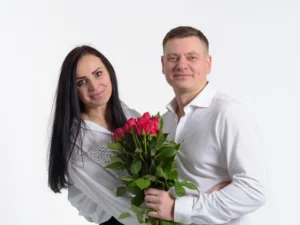 Studio couple’s portrait of a man and woman smiling while holding red roses.
