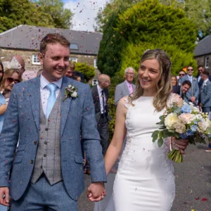 Bride and groom walking through confetti while guests cheer.