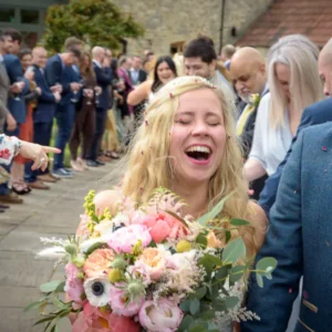 Damien & Laura Wedding 8147-17 square 560px-1  - Bride laughing joyfully during confetti walk at a countryside wedding near Bath, candid wedding photography by Dick Lloyd