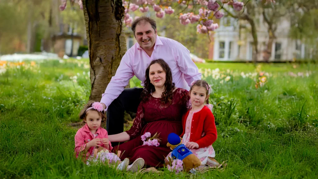 Maternity photography in Harrogate – Iryna with her husband and daughters beneath blossom trees on The Stray, by Dick Lloyd Photography.