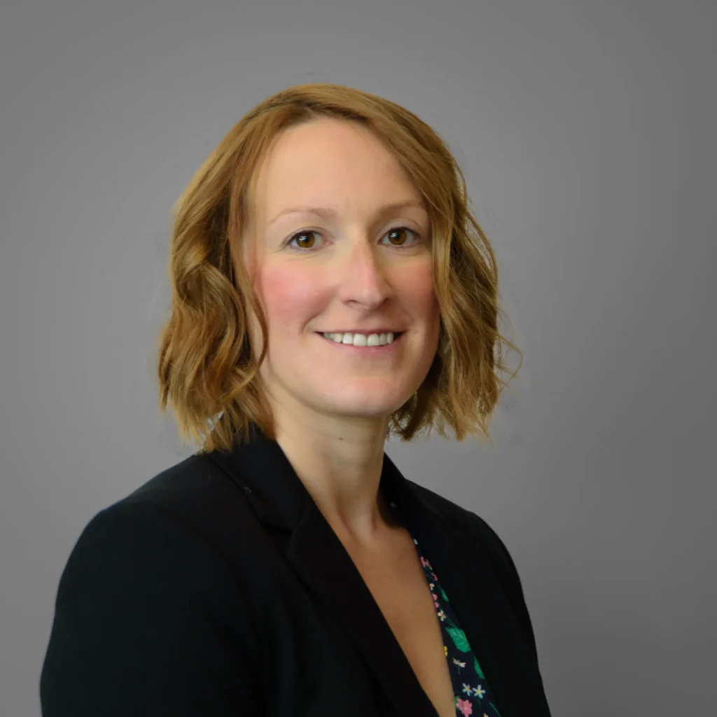 Businesswoman wearing dark top - headshot with grey background Corporate headshot with direct eye contact, illustrating how first impressions are formed quickly in professional contexts