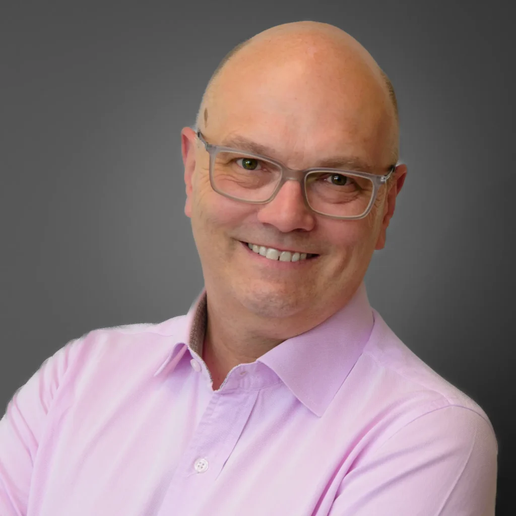 Businessman wearing glasses in pink shirt - corporate headshot with grey background Corporate headshot conveying credibility and professionalism through controlled lighting and confident expression