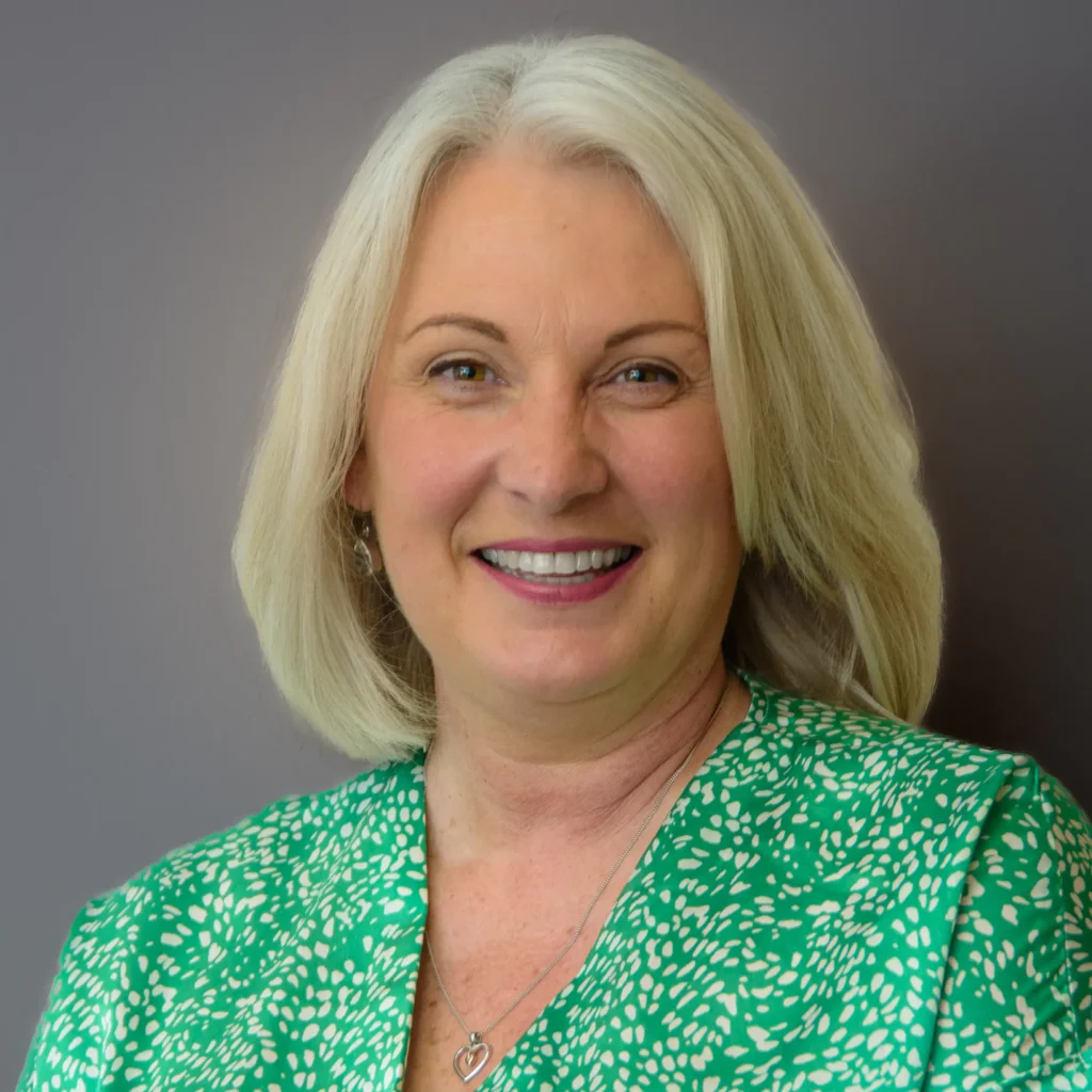 Woman in green dress - headshot with grey background Professional business headshot with a relaxed expression, suitable for modern corporate roles