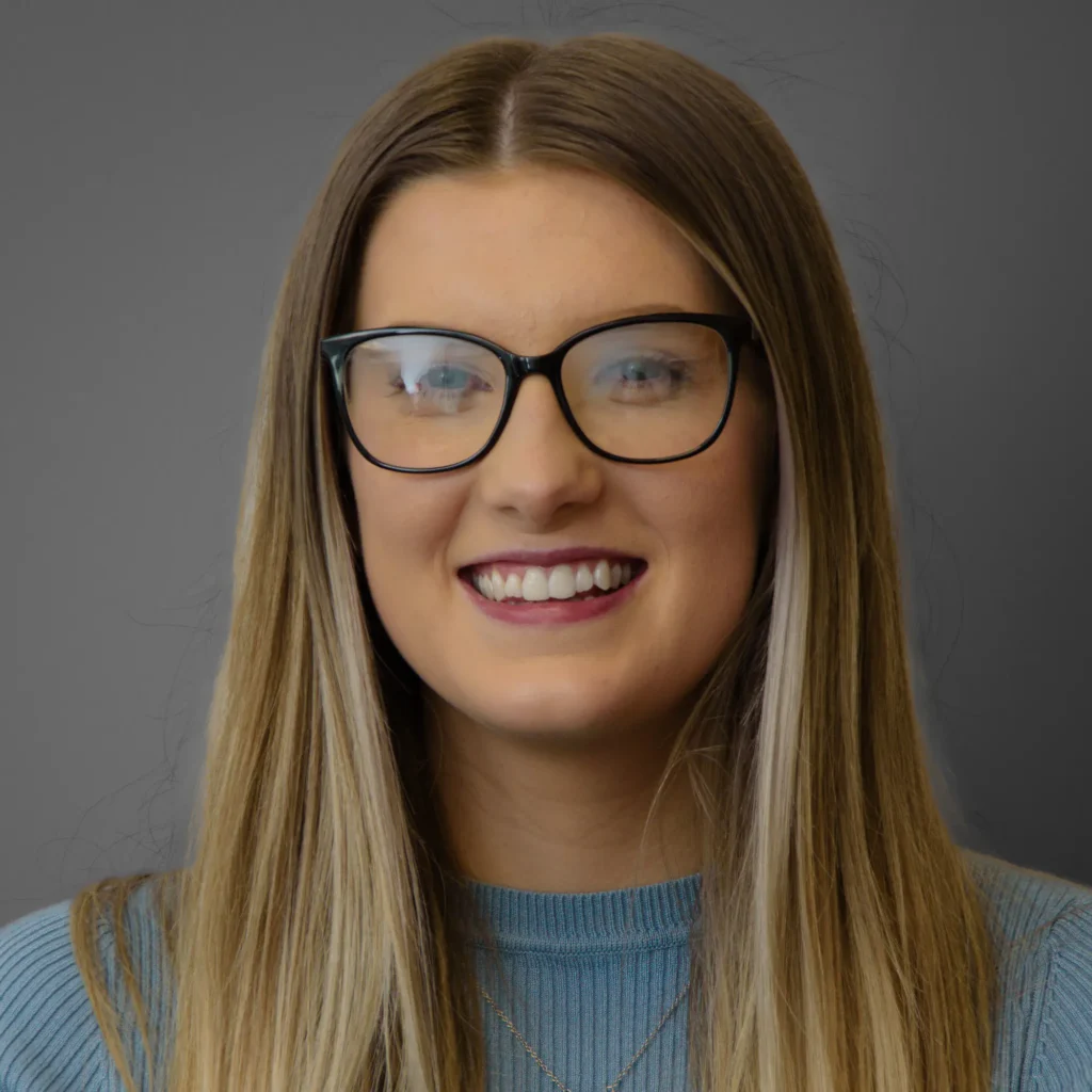 Young business woman wearing blue top and with glasses - corporate headshot with grey background