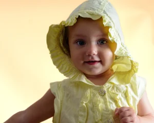 Baby wearing a yellow bonnet softly lit with a yellow background by Dick Lloyd Photography