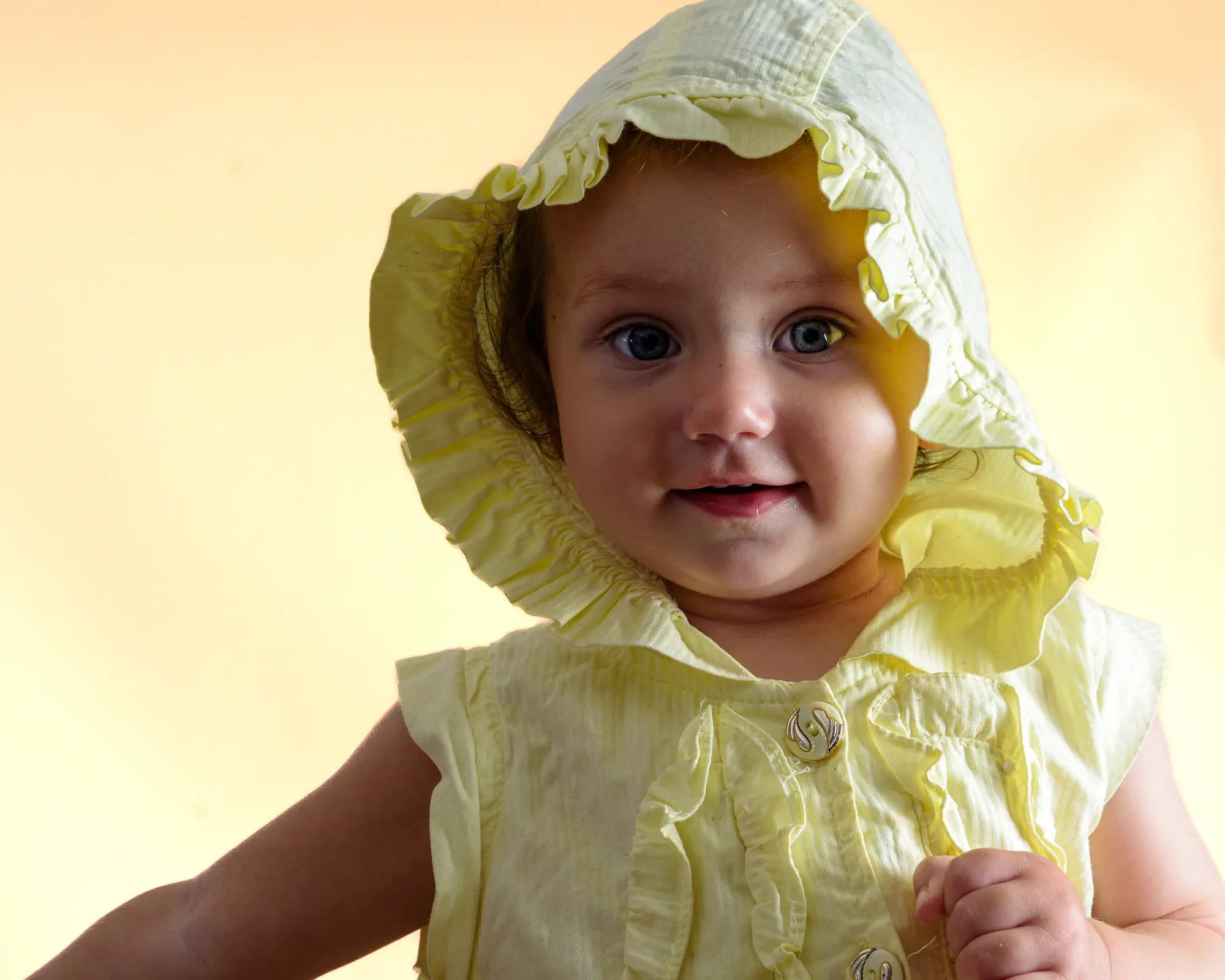 Baby wearing a yellow bonnet softly lit with a yellow background by Dick Lloyd Photography