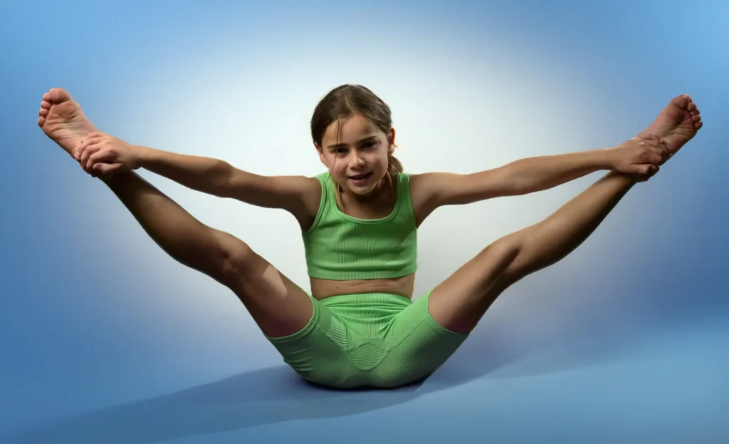 Children’s Photographer Harrogate – Studio Portrait Children’s photographer in Harrogate – studio portrait of a smiling girl stretching in green activewear; playful milestone personality image by Dick Lloyd Photography.