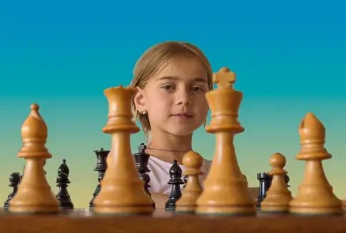 Wide angle studio shot of a young girl behing large chess pieces