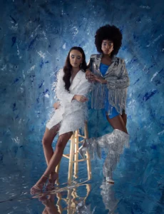 Full-body shot of two female models, one on a stool and one standing with a blue background by Dick Lloyd Photography