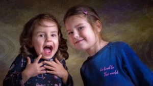 Two sisters having fun, one laughing the other smiling, softly lit with a textured background by Dick Lloyd Photography.