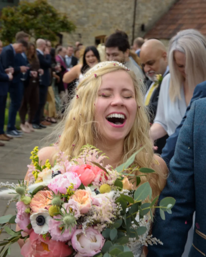Damien & Laura Wedding-8147 Bride laughing and holding bouquet outside after her wedding ceremony, captured in natural light.