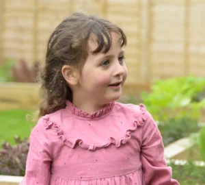 Young girl smiling outdoors in a pink dress during a playful children’s photography session.