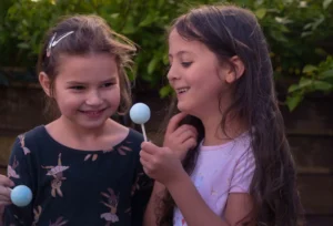 Two joyful young girls giggling with their lollies outdoors