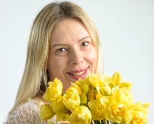 Bright studio portrait of a woman smiling and holding a bouquet of yellow daffodils.