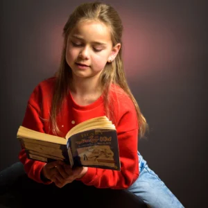 Studio portrait of a young girl wearing a red jumper, reading a book