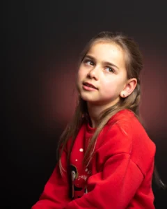 Studio portrait of a young girl with a red jumper with her head turned towards the light source.