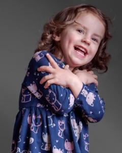 Studio portrait of a young girl laughing with arms crossed playfully across her chest.