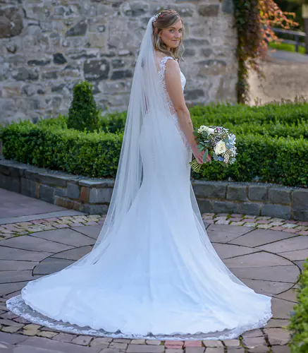 Angharad & Lewis Wedding-1082-Edit Bride standing outside with her veil flowing, holding her bouquet and smiling over her shoulder, captured by Dick Lloyd, Yorkshire Wedding Photographer