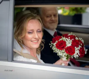 Bride sitting in the wedding car holding her bouquet and smiling.